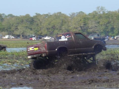 1987 Suzuki Samurai - A lifted pickup truck navigates a muddy obstacle course during a mud bogging event.