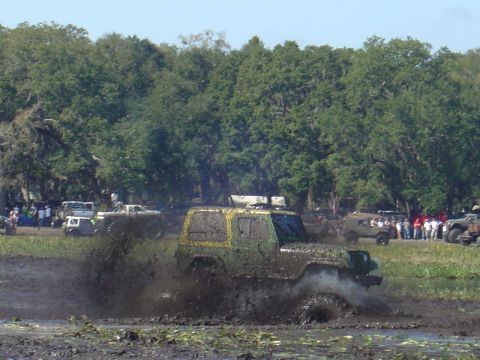 1987 Suzuki Samurai - Several off-road vehicles are seen navigating a muddy terrain with a crowd gathered to watch.