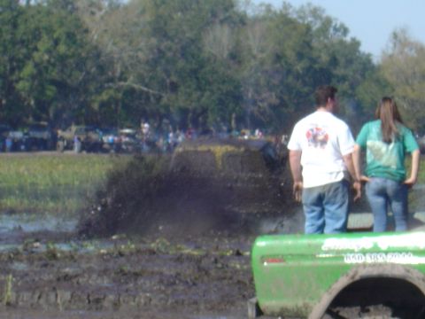 1987 Suzuki Samurai - A yellow SUV is stuck in a mud pit while onlookers observe the scene.
