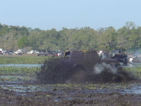 1987 Suzuki Samurai - A truck churns up mud during a bogging event, with spectators and other vehicles visible in the distance.