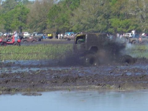 1987 Suzuki Samurai - Multiple vehicles participate in a mud bogging event, kicking up significant spray.