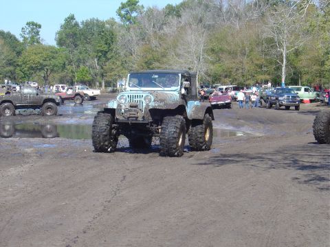 1987 Suzuki Samurai - Multiple off-road vehicles are seen in a muddy area, with a light blue Jeep CJ-5 prominently in the foreground.