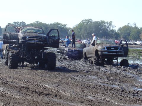 1987 Suzuki Samurai - Several trucks are stuck in the mud during a bogging event, with people standing around and on the vehicles.