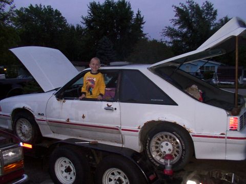 1988 Ford Mustang - White 1988 Ford Mustang on a trailer with hood and trunk open, child in the driver's seat.