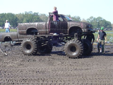 1987 Suzuki Samurai - A lifted pickup truck covered in mud sits in a muddy field, with people around it.