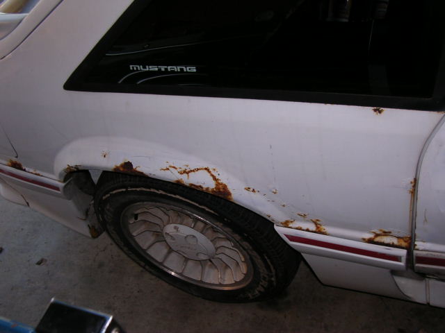 1988 Ford Mustang rear quarter panel with rust and a 'Mustang' decal on the window
