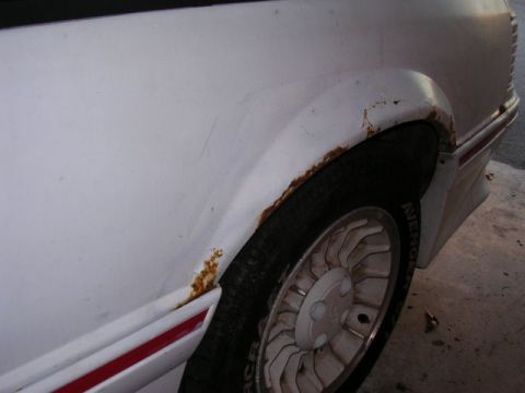 1988 Ford Mustang - Rust is visible around the wheel well of this white vehicle, which has a red stripe on its lower trim.