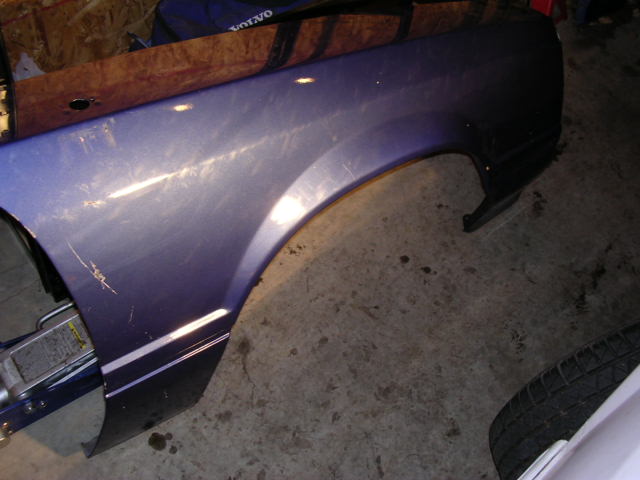 Purple front fender panel lying on garage floor, showing scratches