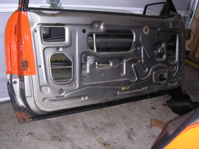 Stripped silver Mustang door shell with orange edge standing in a garage, inner panel exposed