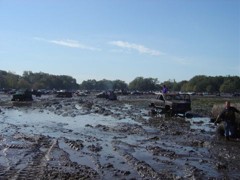 1987 Suzuki Samurai - A muddy field filled with vehicles, some stuck in the mud, under a clear blue sky.