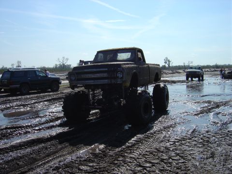1987 Suzuki Samurai - Monster truck driving through a muddy field with other vehicles present.