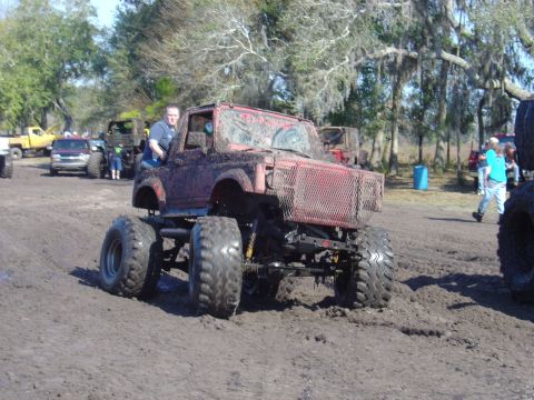 1987 Suzuki Samurai - A modified 1987 Suzuki Samurai navigates a muddy track with other vehicles in the background.