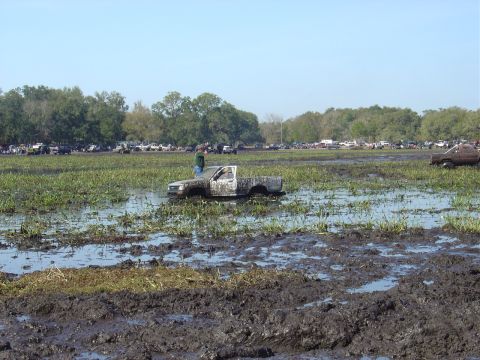 1987 Suzuki Samurai - A white pickup truck is stuck in a muddy field with several other vehicles visible in the background.