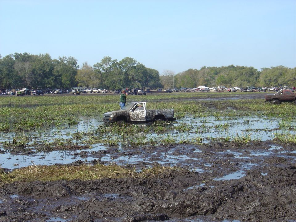White pickup truck stuck in mud with a person standing on it