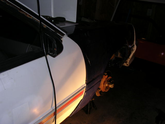 White 1988 Ford Mustang side view, rear wheel removed and car on jack stands. Red stripe along lower body