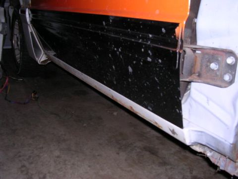 1988 Ford Mustang - Detail of a car door, showing the lower black section with white specks and an exposed metal hinge mechanism.