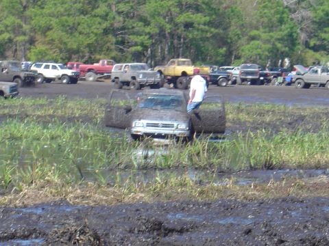 1987 Suzuki Samurai - A muddy scene with several trucks, one of which is stuck in the mire with its doors ajar.