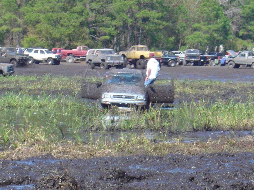 Truck stuck in mud with doors open, person standing by it. Other trucks in background