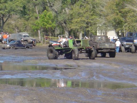 1987 Suzuki Samurai - Multiple off-road vehicles navigate a muddy terrain, with spectators visible in the distance.