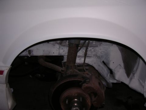 1988 Ford Mustang - Close-up of the front wheel well of a white 1988 Ford Mustang, showing suspension and brake details.