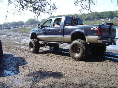1987 Suzuki Samurai - A lifted pickup truck navigates a muddy terrain, with "4x4 OFF ROAD" branding visible.