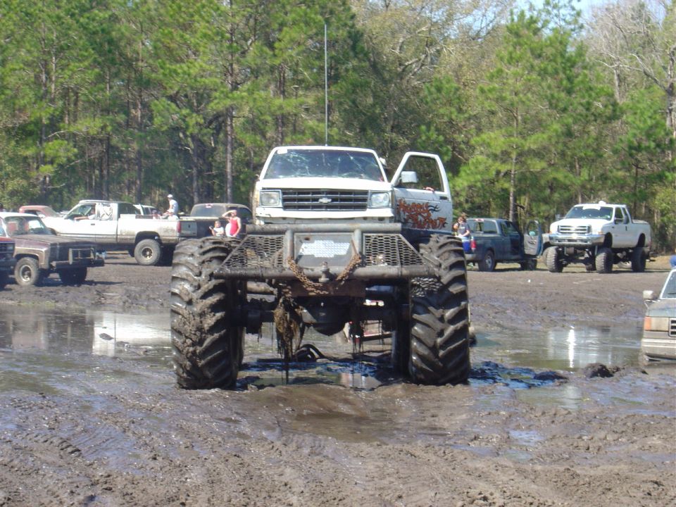 Monster truck with huge tires in mud, other trucks around