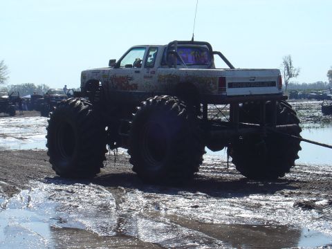 1987 Suzuki Samurai - A modified truck with oversized tires sits in a muddy area, possibly at an event.