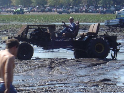 1987 Suzuki Samurai - A custom-built off-road vehicle navigates a muddy terrain, with spectators and other vehicles visible in the background.