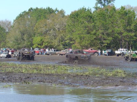 1987 Suzuki Samurai - Several trucks are engaged in a mud bogging event, kicking up large amounts of mud as they drive through the mire.