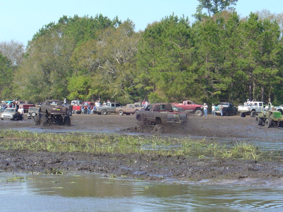 Mud bogging scene with multiple trucks splashing through a muddy field