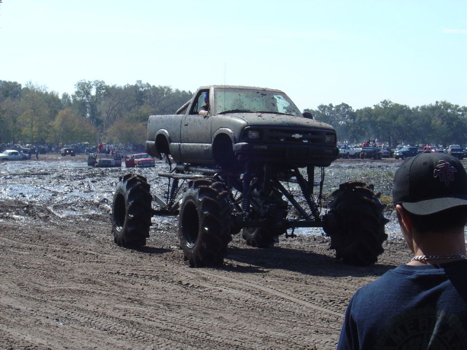 Monster truck with huge tires in mud pit, crowd in background
