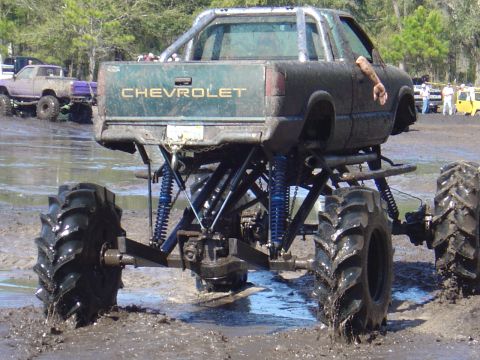 1987 Suzuki Samurai - A heavily modified Chevrolet pickup truck navigates a muddy terrain with its large, aggressive tires.