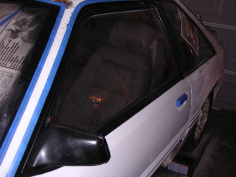 1988 Ford Mustang - The interior of a white 1988 Ford Mustang is visible through the window, with masking tape applied to the window frame.