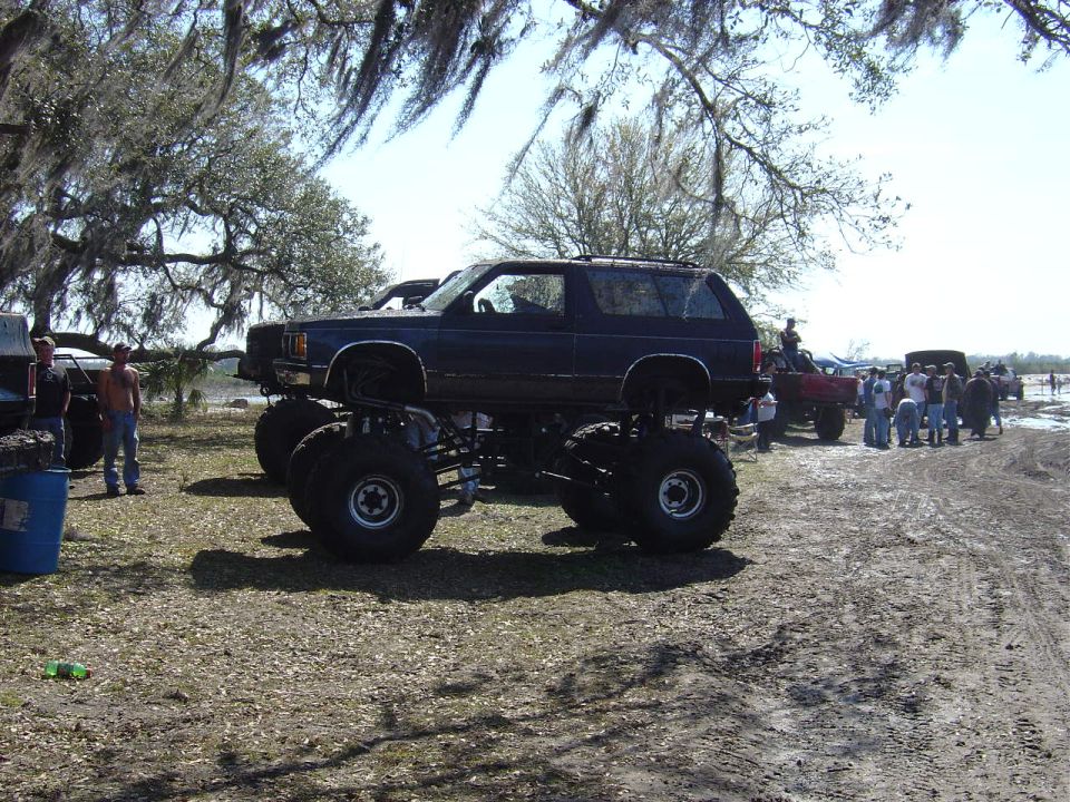 Dark blue monster truck with large tires parked on dirt