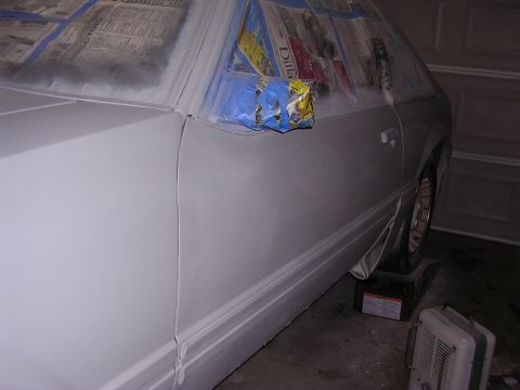 1988 Ford Mustang - A white car is being prepped for paint, with windows covered and the body taped and masked.