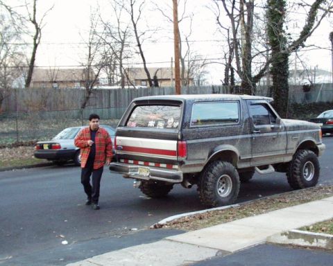 1989 Ford Bronco - A man walks past a lifted Ford Bronco parked on a residential street.