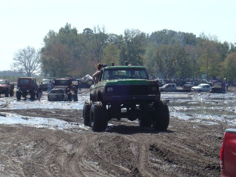 1987 Suzuki Samurai - Mud bogging event with multiple vehicles stuck in the mud under a clear sky.