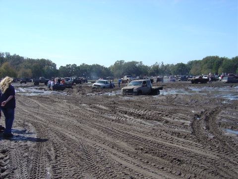 1987 Suzuki Samurai - A muddy field is filled with trucks, some of which are stuck deep in the mud.