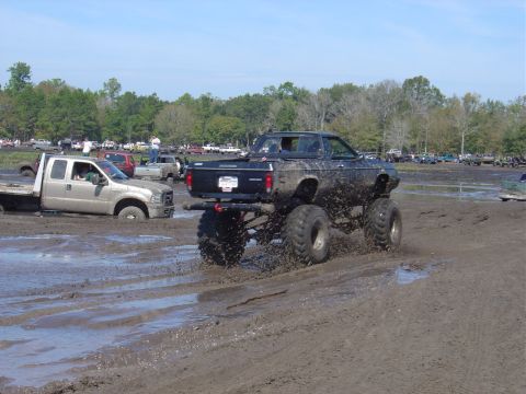 1987 Suzuki Samurai - A black monster truck navigates a muddy terrain, while another vehicle is stuck in the mire.