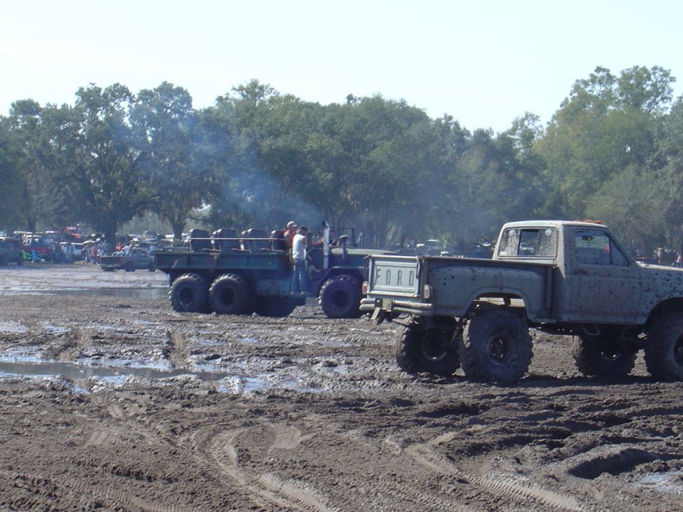 Muddy Ford pickup truck and a multi-wheeled vehicle in a mud pit with trees in the background