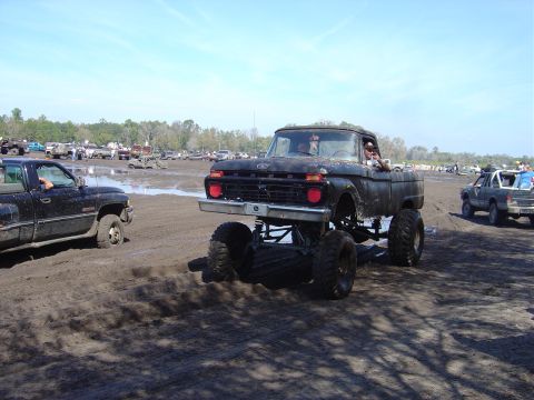 1987 Suzuki Samurai - This lifted pickup truck is participating in a mud bogging event with other vehicles in the background.