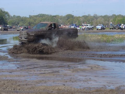 1987 Suzuki Samurai - A truck churns up mud as it navigates a wet terrain, with other vehicles and onlookers present.