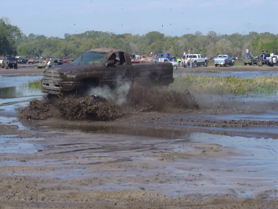 Mud-splattered truck driving through a muddy field with spectators in the background