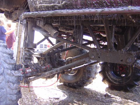 1987 Suzuki Samurai - The undercarriage of a heavily modified off-road vehicle is covered in mud, with large, aggressive tires visible.