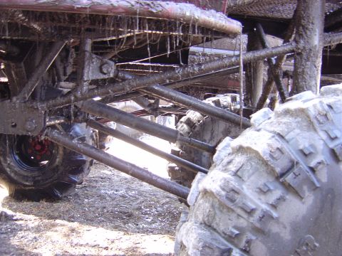 1987 Suzuki Samurai - Close-up view of the heavily muddied suspension and tires of an off-road vehicle.