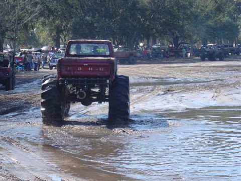 1987 Suzuki Samurai - A modified Ford pickup truck navigates a muddy terrain, with spectators and other vehicles present.