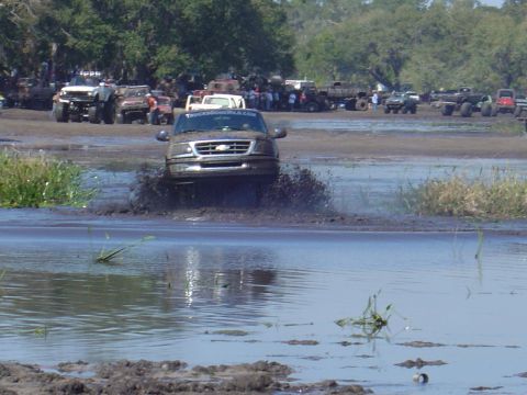 1987 Suzuki Samurai - Ford F-150 navigates a muddy obstacle course with other vehicles and spectators present.