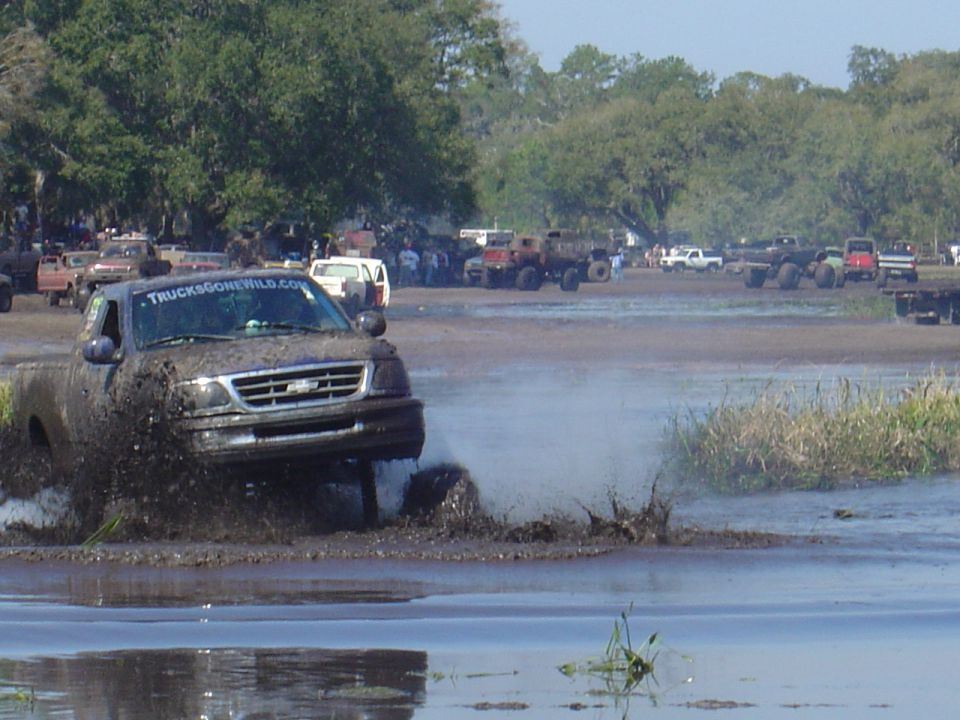Truck splashing through mud, with other vehicles and spectators in the background