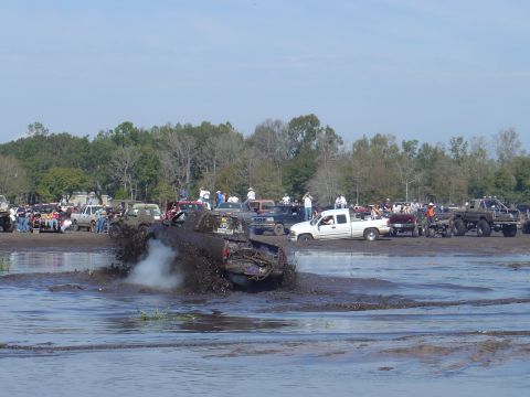 1987 Suzuki Samurai - Multiple trucks are engaged in a mud bogging competition, with spectators gathered around the muddy track.