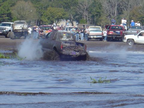 1987 Suzuki Samurai - Trucks participate in a mud bogging event, kicking up water and mud.